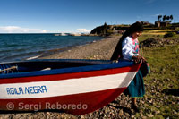 Una mujer de la isla de Amantaní vestida con su traje típico regional junto a una barca a los pies del Lago Titicaca. 